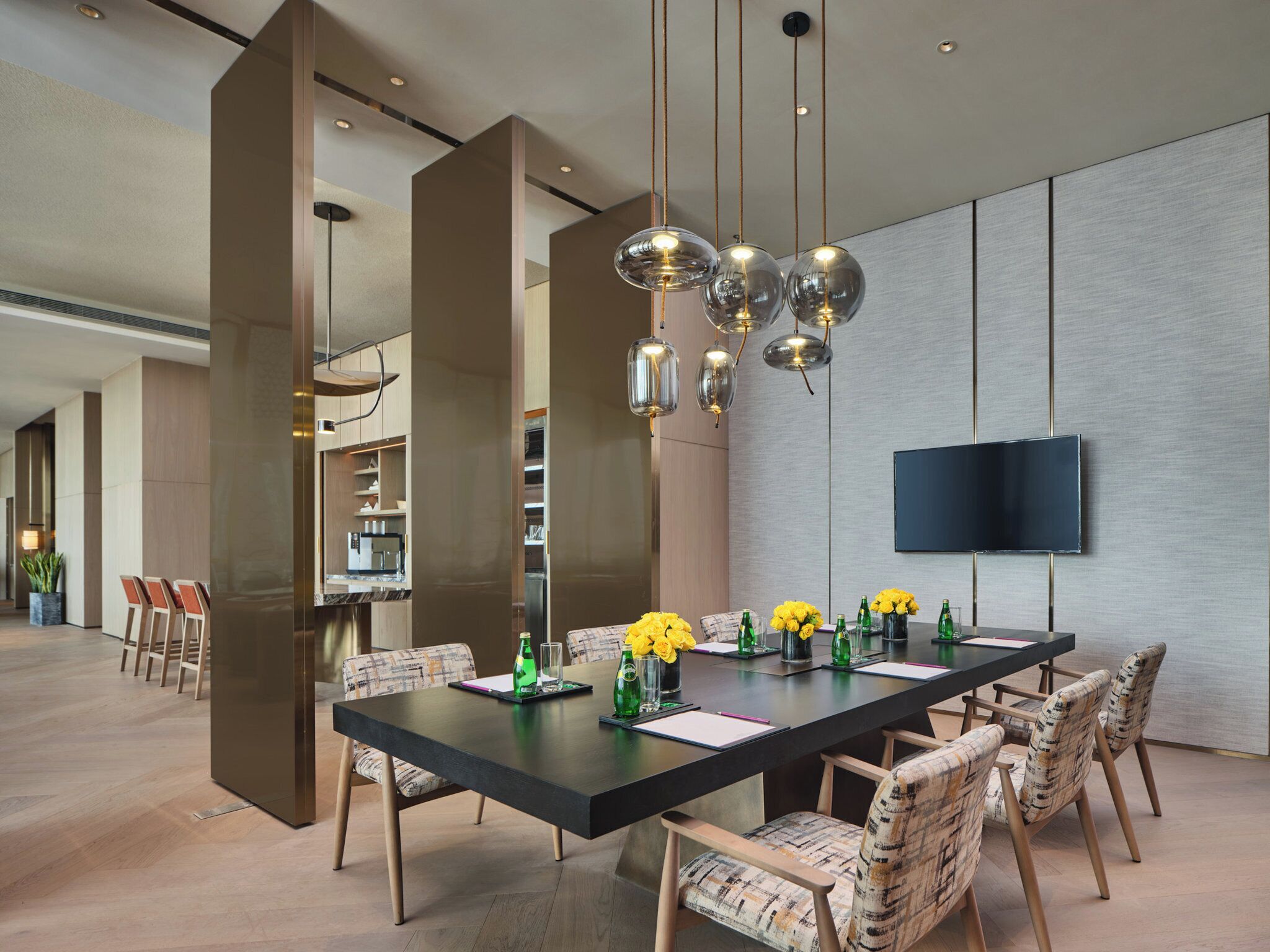 Un espace repas moderne avec une longue table, des chaises et un téléviseur fixé au mur.