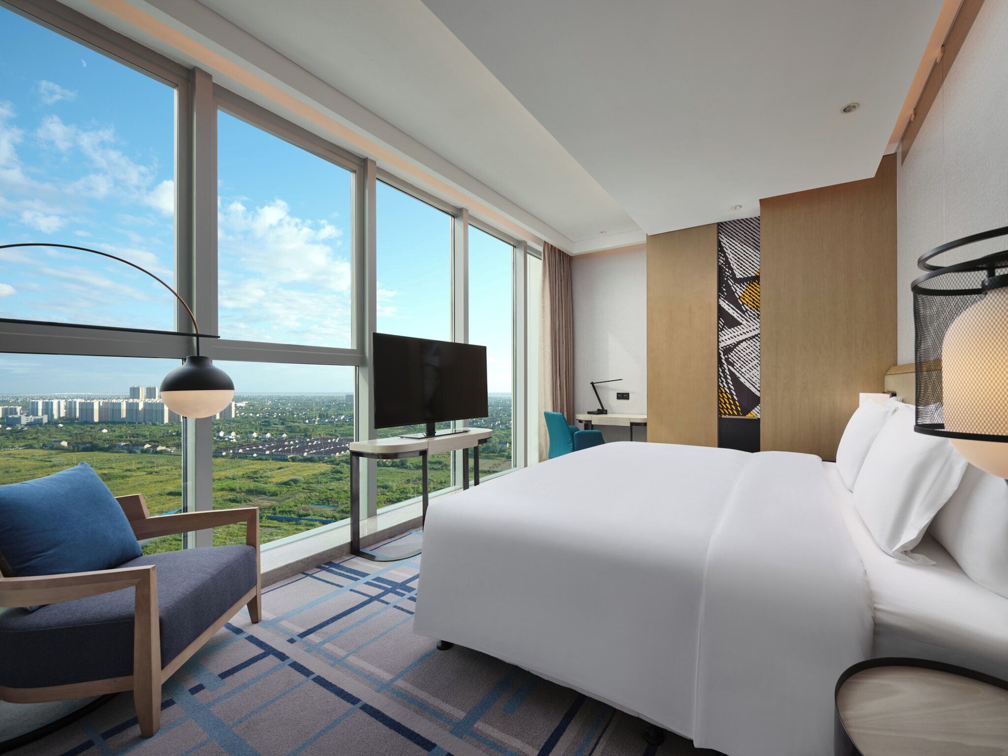 A hotel room with a large bed, a TV, a desk, and a view of a cityscape.