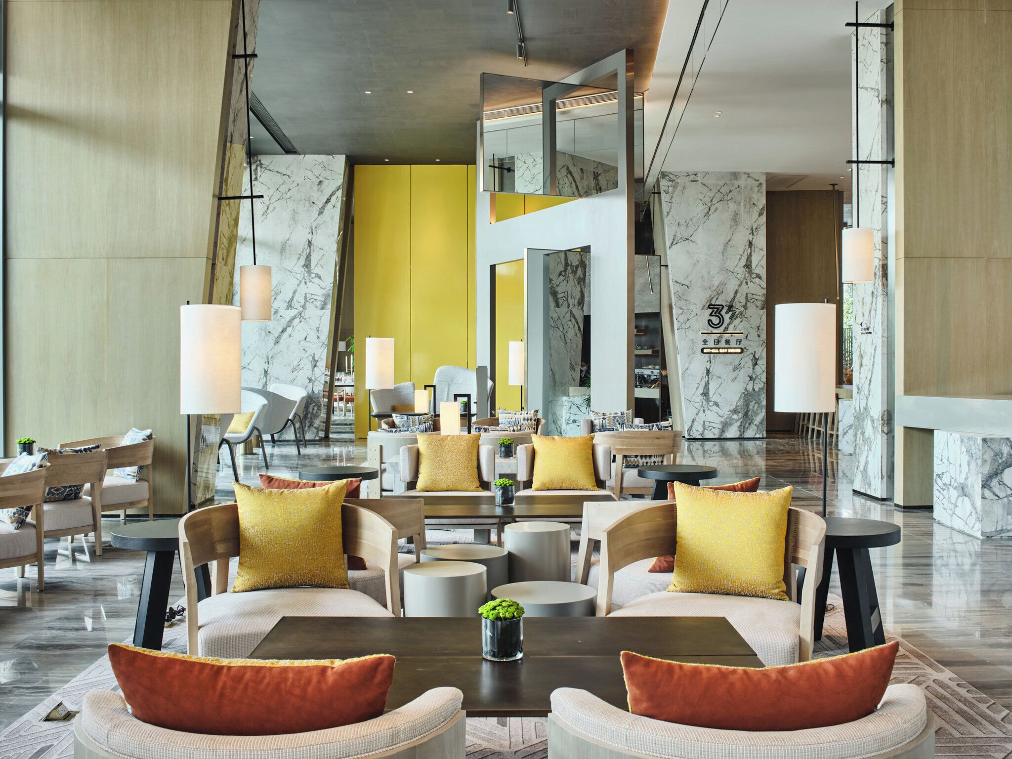 A modern hotel lobby with a central seating area, a reception desk, and a view of the interior.