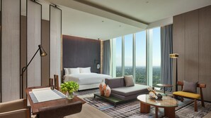 Een moderne hotelkamer met een groot bed, een bank, een eettafel en uitzicht op de stad door grote ramen.