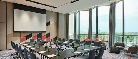 A conference room with a large table, chairs, a projector screen, and a view of the city through large windows.