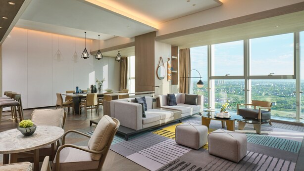 Een moderne woonkamer met een bank, stoelen, een eethoek en grote ramen met uitzicht op de stad.