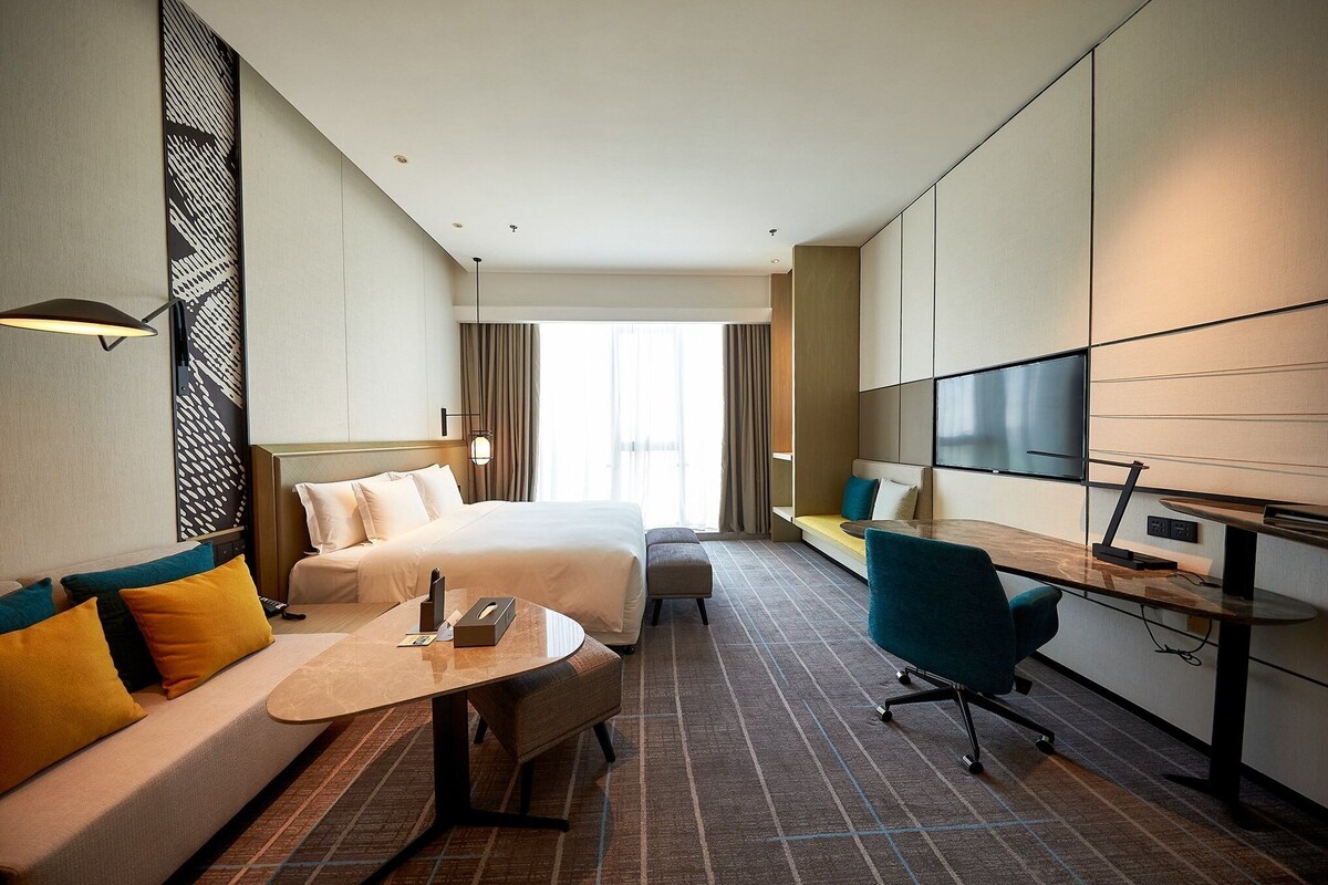 Een hotelkamer met een bed, een bank, een bureau, een stoel, een televisie en een groot raam.