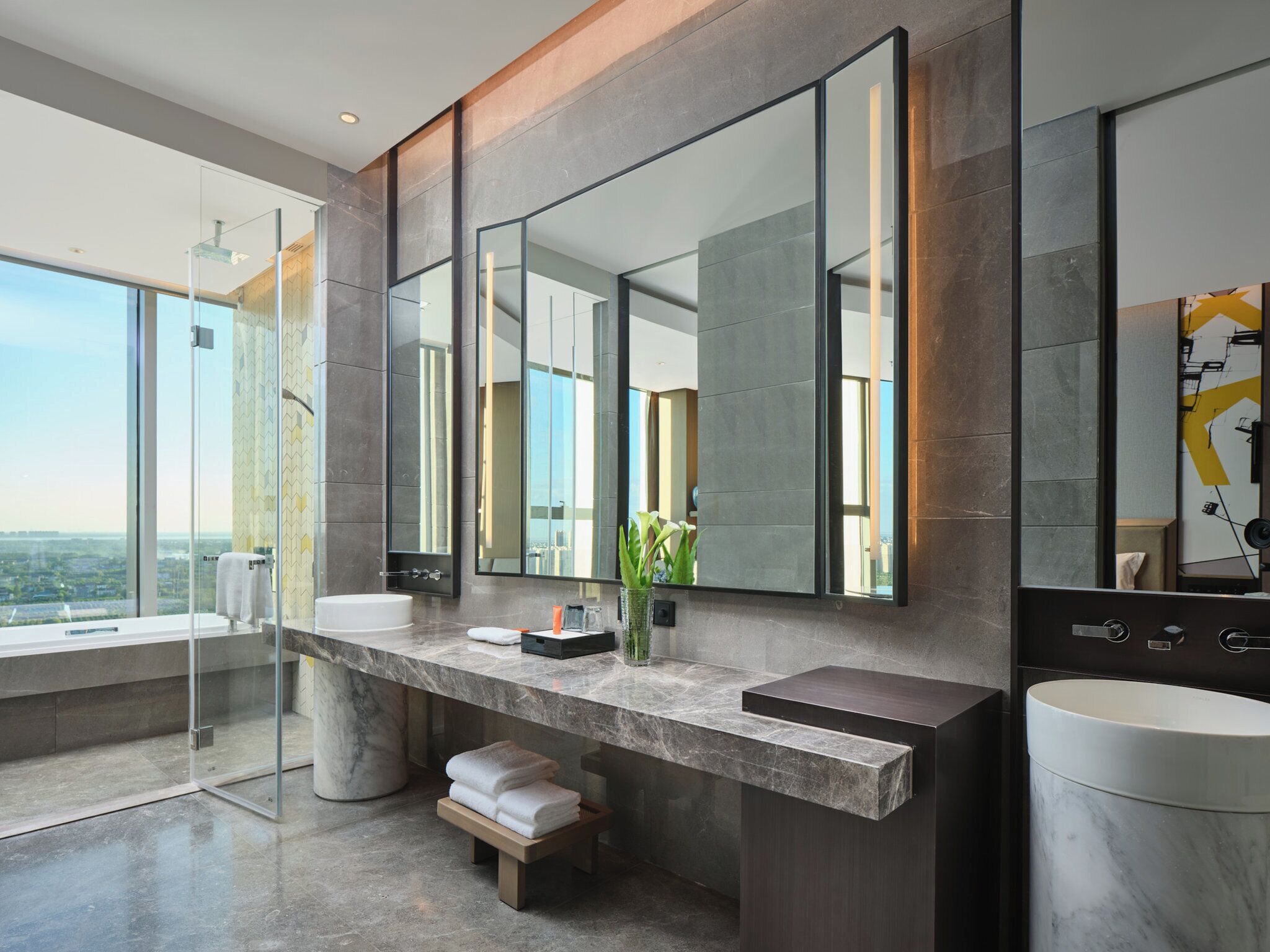 Un baño moderno con un espejo grande, dos lavamanos y un banco.