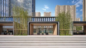 Een modern gebouw met een glazen gevel, een overdekt terras en een trap die naar de ingang leidt.