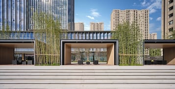 Un edificio moderno con fachada de vidrio, una zona de estar al aire libre cubierta y una escalera que conduce a la entrada.