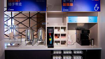 Un espace dédié au café, équipé d’une machine à café, d’un menu numérique présentant les différentes variétés de café et d’un présentoir à tasses.