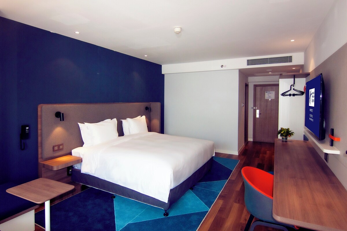 Una habitación de hotel moderna con una cama grande, una mesita de noche y un escritorio con una silla.