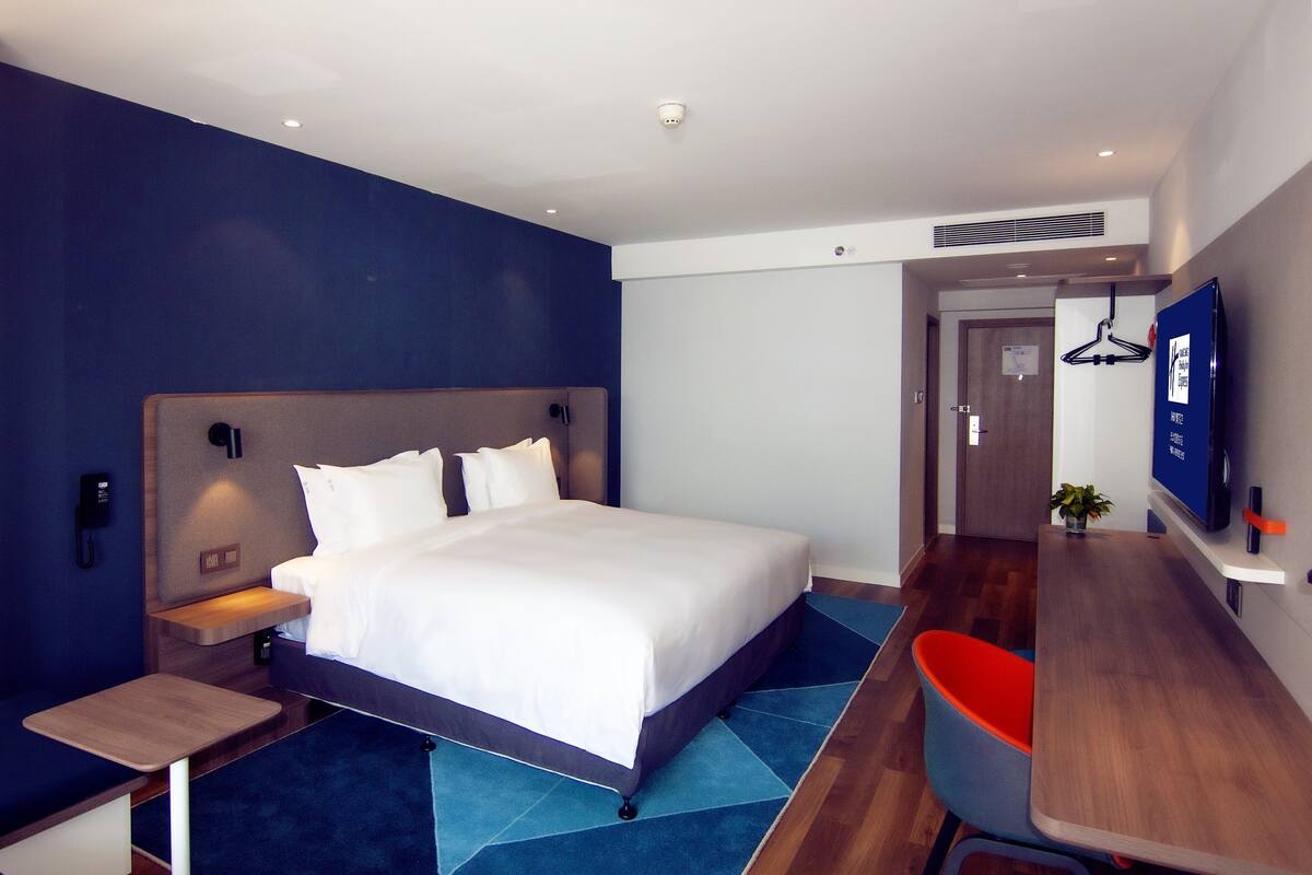 Una habitación de hotel moderna con una cama grande, una mesita de noche y un escritorio con una silla.