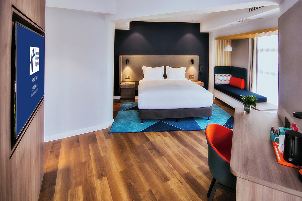 Habitación de hotel moderna con una cama grande, un escritorio con silla y vistas a la ciudad desde la ventana.