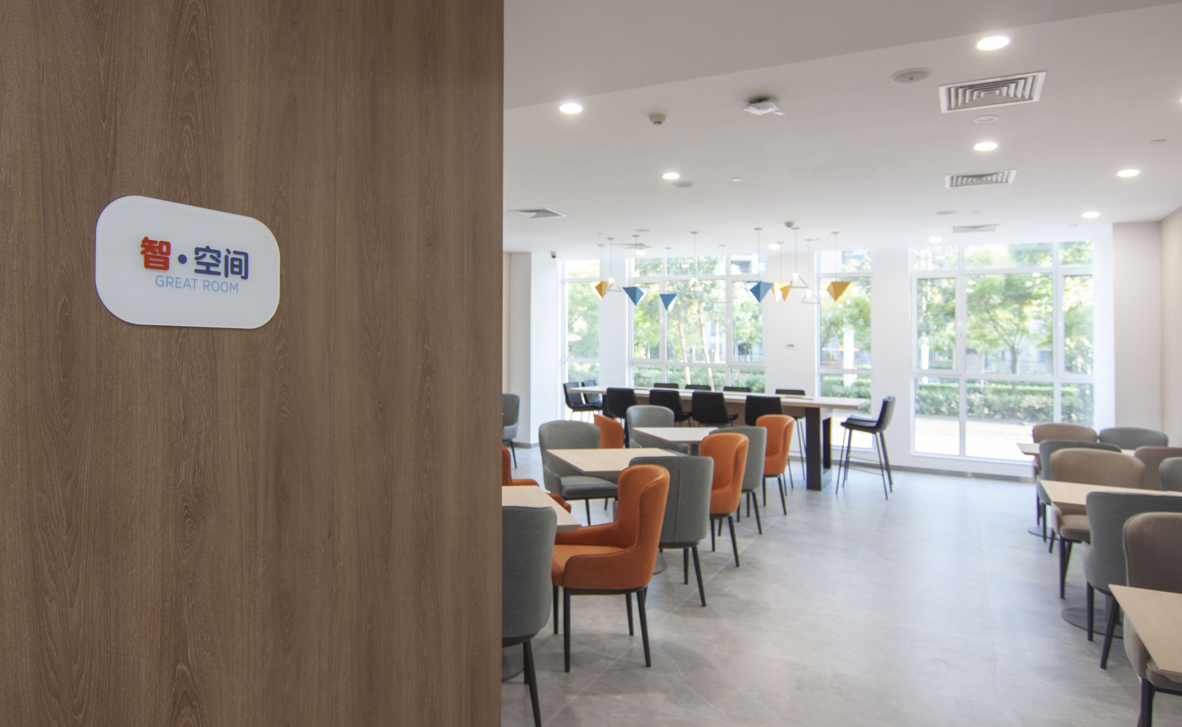 Ein moderner Essbereich mit Tischen und Stühlen, großen Fenstern und einem Schild, das einen 'Great Room' bezeichnet.