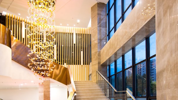 Un hall d’hôtel moderne avec un escalier en marbre, un luminaire décoratif et de grandes fenêtres.