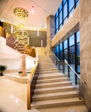Un hall d’hôtel moderne avec un escalier en marbre, un luminaire décoratif et de grandes fenêtres.