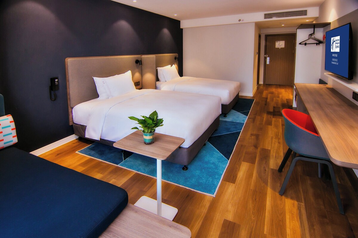 Habitación de hotel con dos camas, un escritorio, un televisor y una planta.
