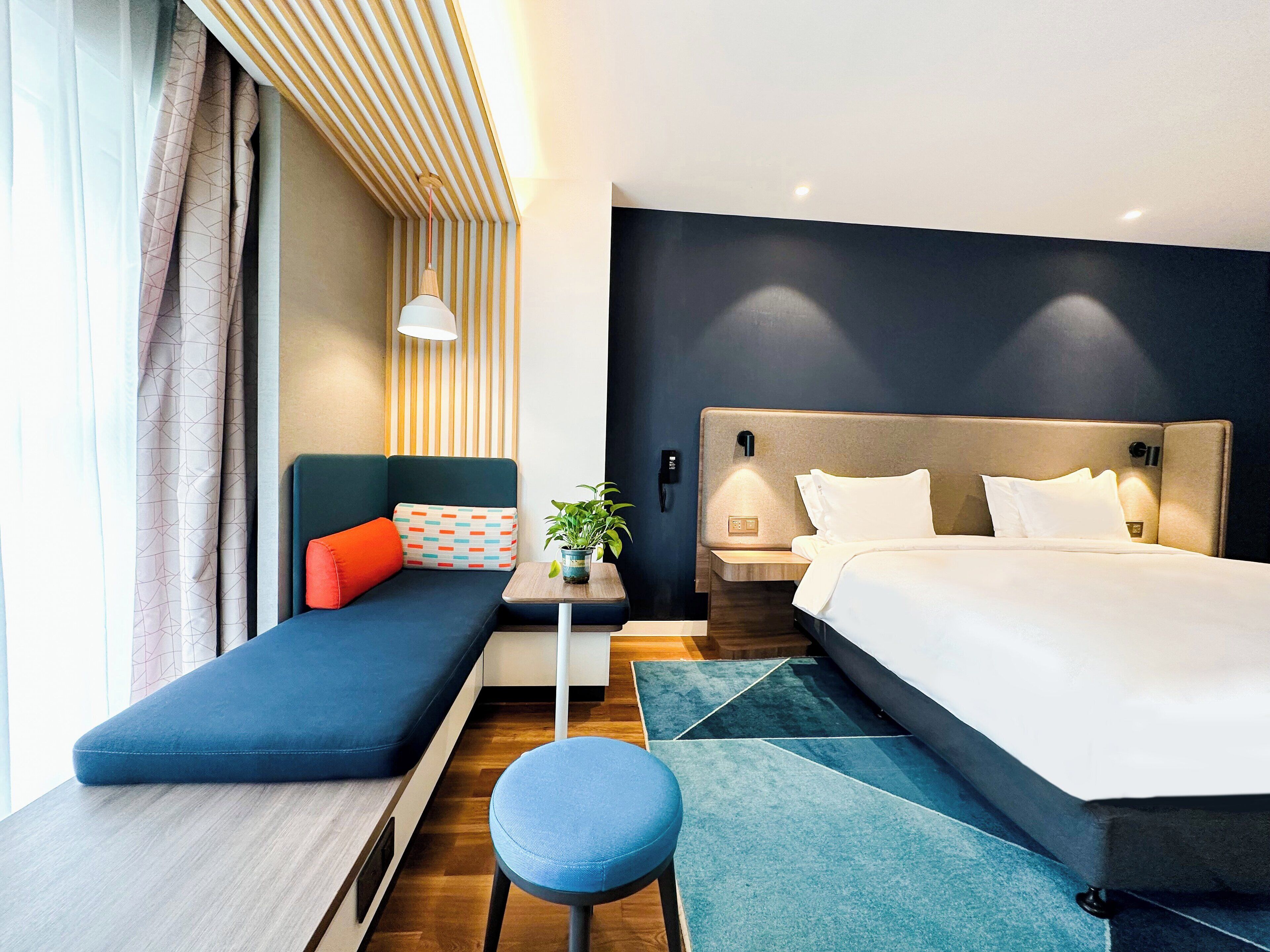 Een moderne hotelkamer met een bed, een bank, een tafeltje met een plant en een nachtkastje.