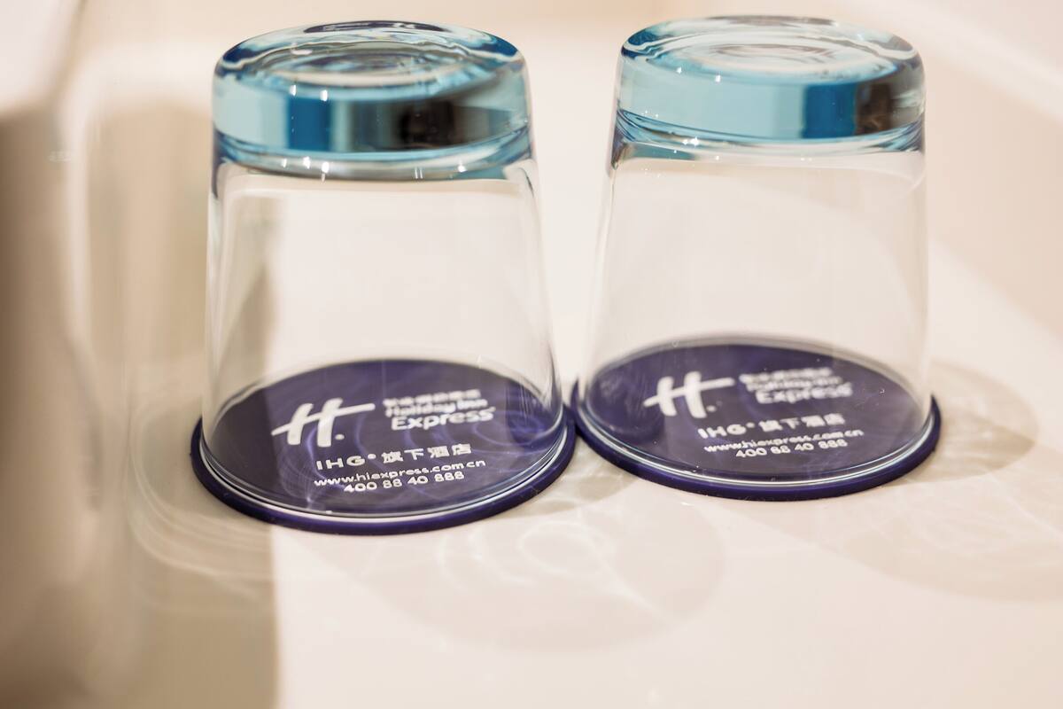 Dos recipientes de vidrio transparente con tapas azules y etiquetas, sobre una superficie blanca.