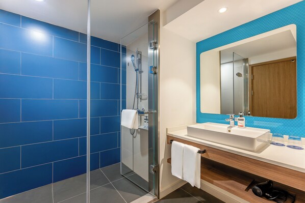 Une salle de bain moderne avec des carreaux bleus, une douche en verre, un lavabo blanc et un meuble-lavabo en bois.