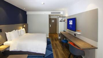 Une chambre d’hôtel comprenant un lit, un bureau, une chaise, un téléviseur et une porte donnant sur une autre pièce.