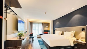 Une chambre d’hôtel moderne dotée d’un grand lit, d’un bureau avec une chaise, d’une télévision et d’un petit coin salon avec un canapé et une table.