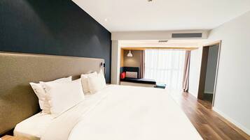 Una habitación de hotel moderna con una cama grande, una mesita de noche, cortinas en la ventana y una puerta que da a otra habitación.