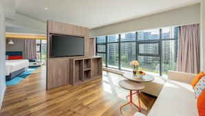 Une chambre d’hôtel moderne dotée d’une grande télévision, d’un canapé, d’une table à manger et offrant une vue sur la ville grâce à de grandes fenêtres.