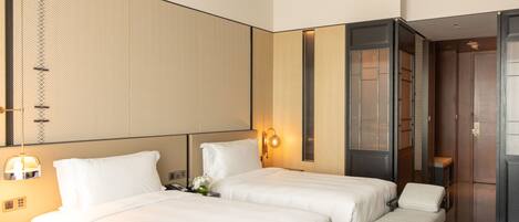 A hotel room with two beds, a bench, a mirror, a wall-mounted light, and a wardrobe.