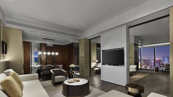 A modern hotel room with a large bed, a round coffee table, a TV, and a city view.