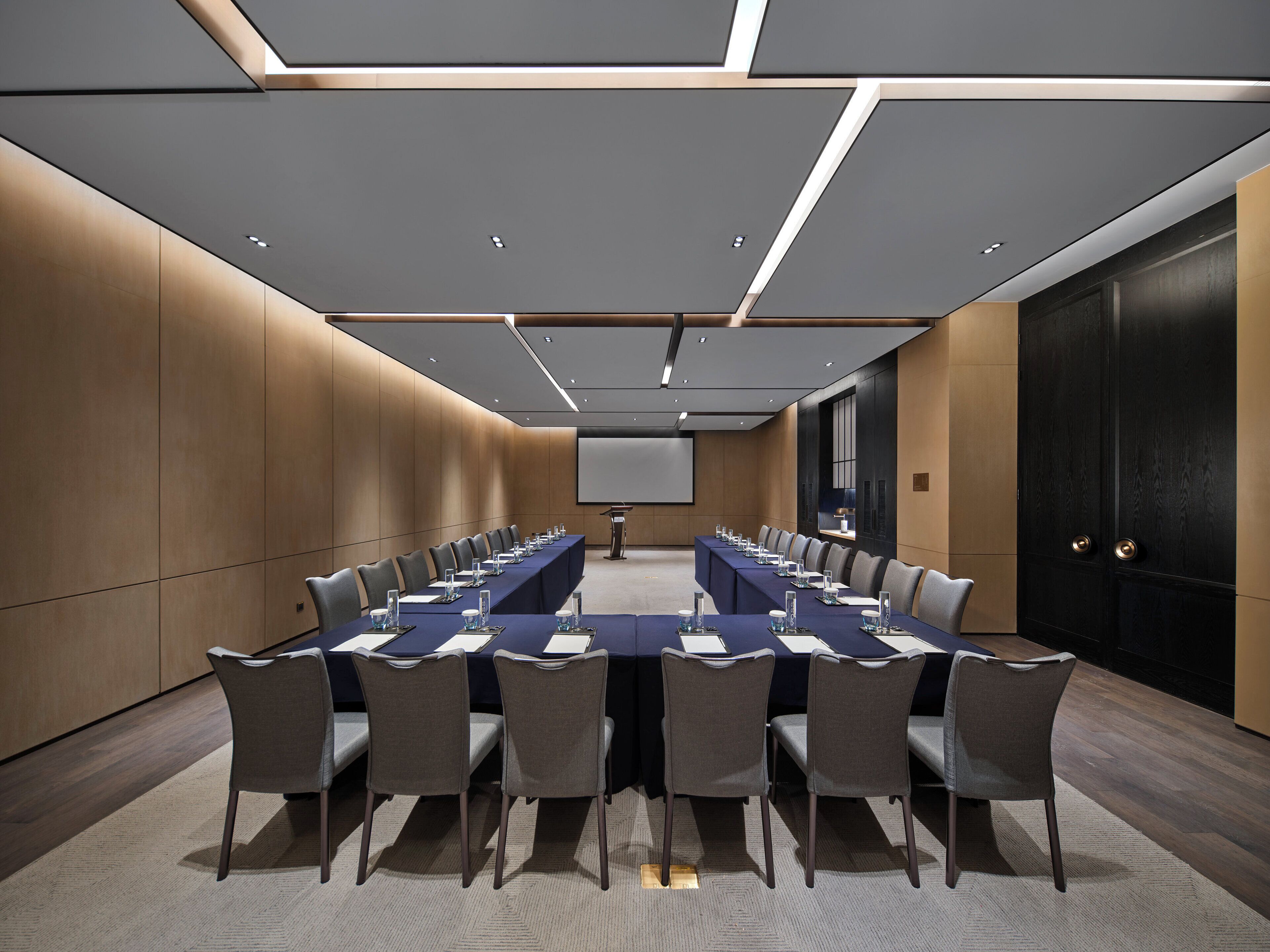 A conference room with a long table, chairs, a projector screen, and a door.
