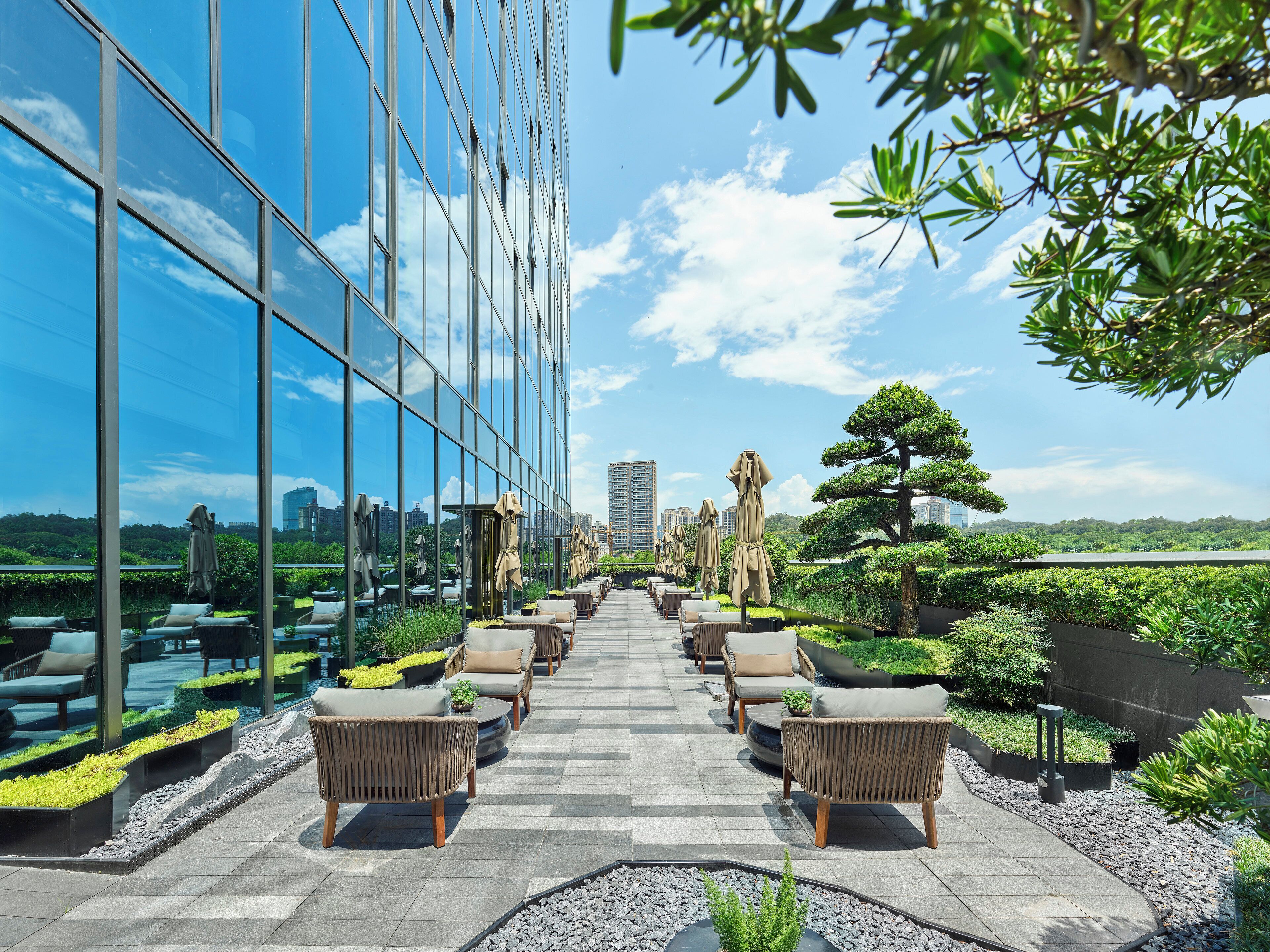 A rooftop terrace with outdoor seating, a glass building facade, and a view of the city skyline.