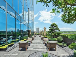 Una terraza en la azotea con mobiliario exterior, fachada de vidrio de un edificio y vista del horizonte urbano.