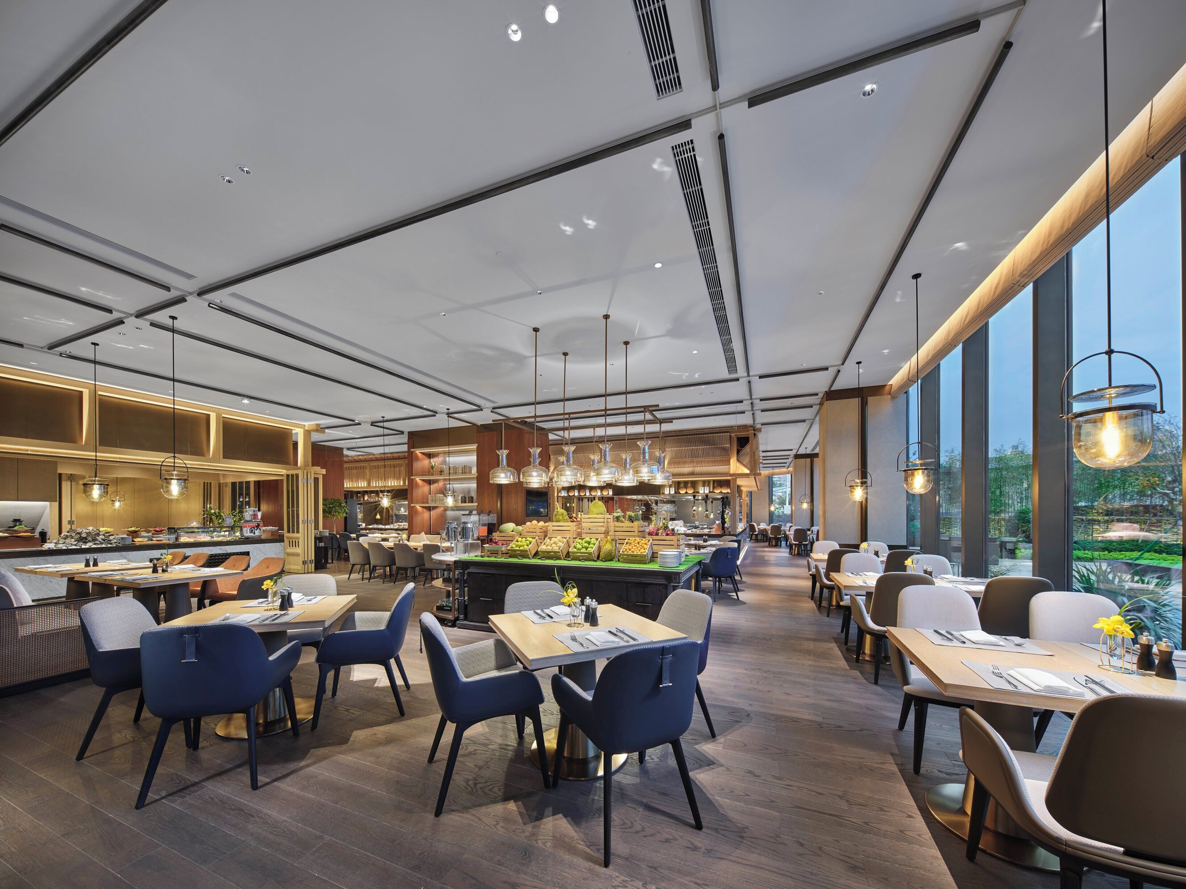 A modern restaurant interior with high ceilings, pendant lighting, and a central dining area with tables and chairs.