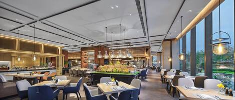 Un interior de restaurante moderno con techos altos, iluminación colgante y una zona de comedor central con mesas y sillas.