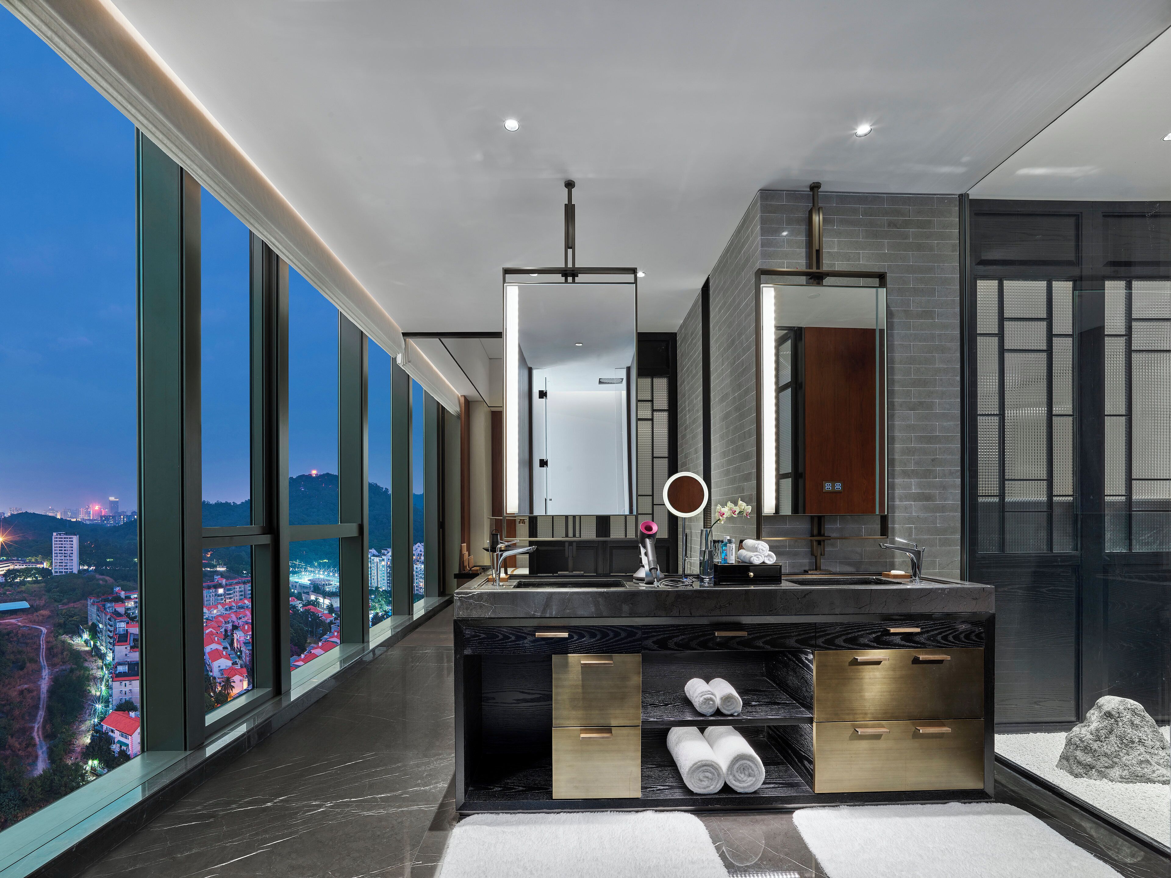 A modern bathroom with a large window, a vanity with a mirror, and towels.
