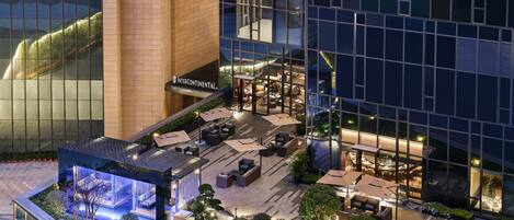 A modern hotel with a rooftop terrace, outdoor seating, and a well-lit entrance.