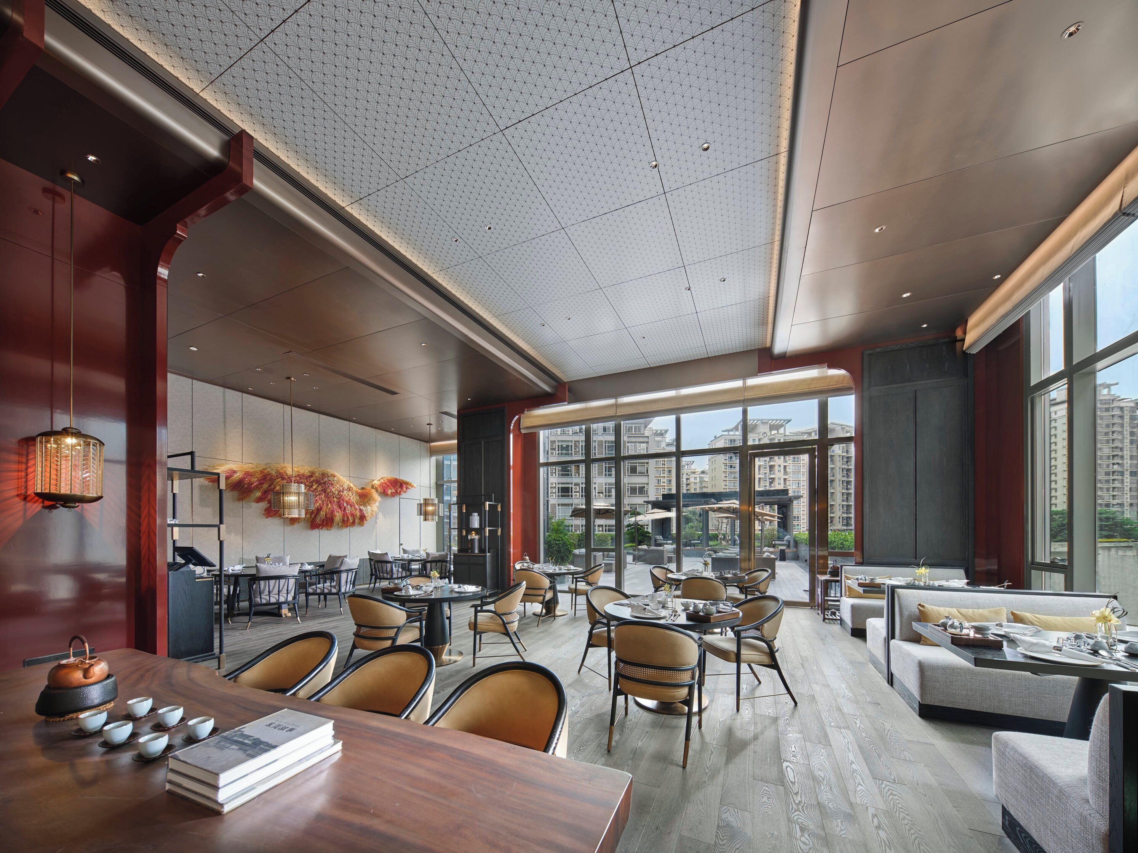 Un comedor amplio con varias mesas y sillas, ventanas grandes que ofrecen vistas del paisaje urbano y un techo con diseño decorativo.