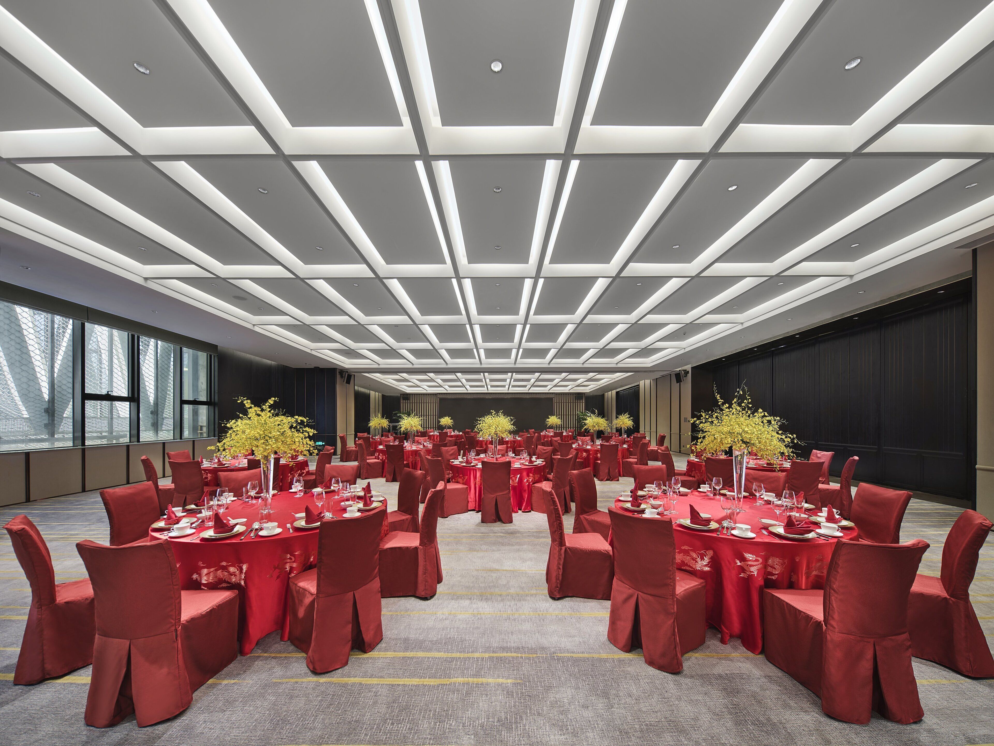 A large conference room with tables set for a formal event, featuring a modern ceiling design and large windows.