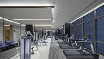 Un gimnasio moderno con cintas de correr, máquinas de pesas y un espejo grande.