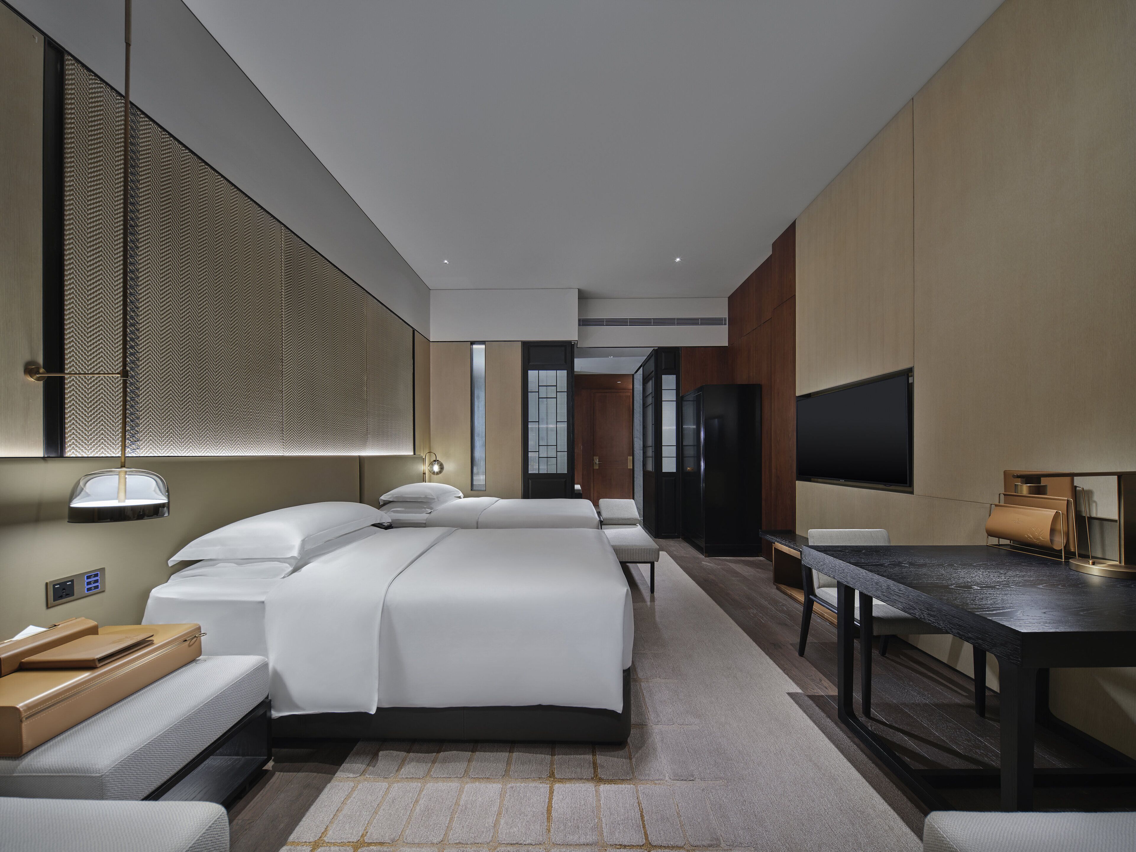Una habitación de hotel moderna con una cama grande, mesitas de noche, un escritorio y un televisor.