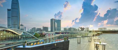 A rooftop bar with a view of the city skyline, featuring modern buildings and a clear sky.