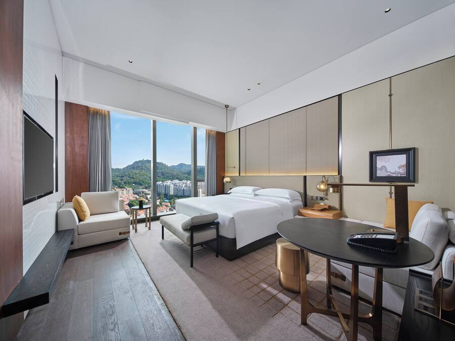 A modern hotel room with a large bed, a sofa, a dining table, and a TV.