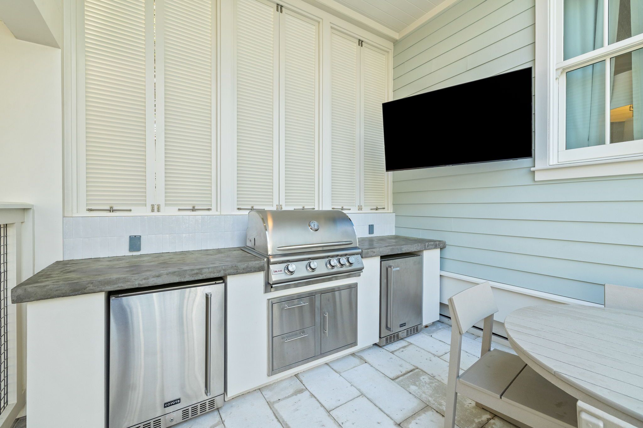 A compact kitchen with a built-in grill, a small refrigerator, and a window with blinds.