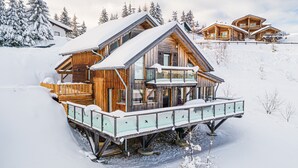 Una cabaña de madera con balcón, rodeada de árboles cubiertos de nieve y un cielo despejado.