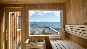 Una cabaña de madera con un ventanal grande que ofrece vistas a la montaña. En el interior, hay un banco y una pequeña mesa.