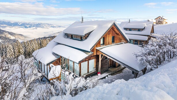 Una cabaña de madera con techo inclinado, ventanas amplias y vistas a montañas nevadas.
