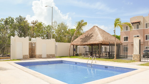Uma piscina com cobertura de palha, cercada por um muro branco e uma grade.