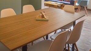 Uma área de refeições com mesa e cadeiras de madeira, um sofá azul com almofadas coloridas e um lustre.