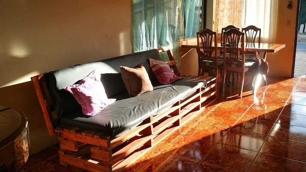 A wooden sofa with cushions, a dining table with chairs, and patterned floor tiles. - Guesthouse Morpho CR (Quepos)