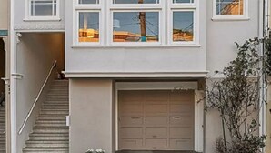 A two-story building with a garage, multiple windows, and a staircase leading to the entrance.