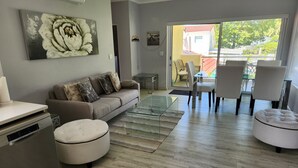 Ein Wohnzimmer mit Sofa, Hocker, Glastisch und einem Bild an der Wand.