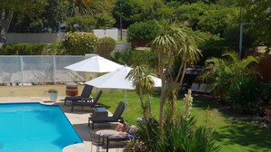 Ein Swimmingpool mit Liegestühlen und Sonnenschirmen, umgeben von einer gepflegten Rasenfläche und verschiedenen Pflanzen.
